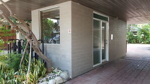 A building with a brick exterior, a glass door, and a small garden area with plants and a tree. - The Riverside Hotel & Motel (Kaohsiung)