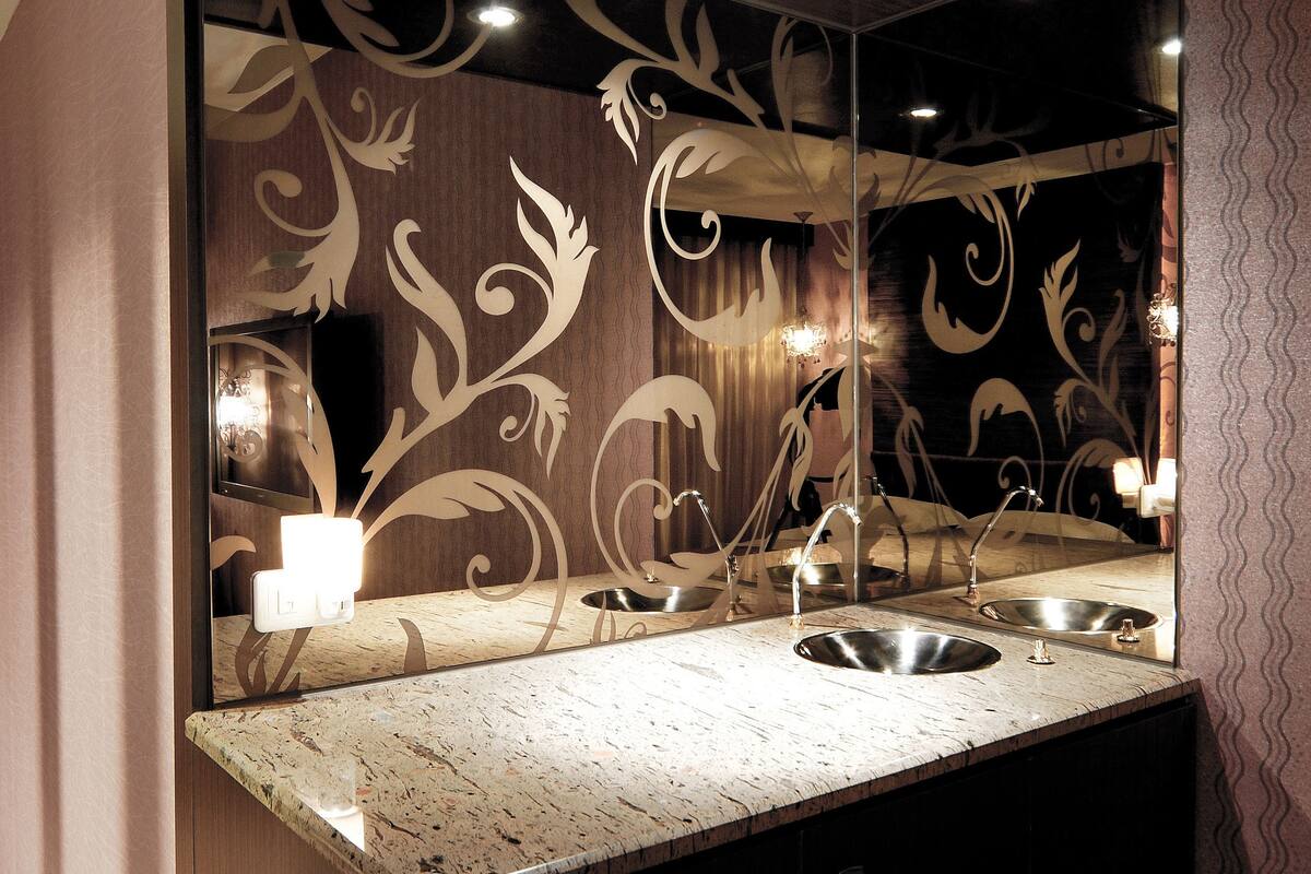 A bathroom with a large mirror, two sinks, and decorative wall patterns.