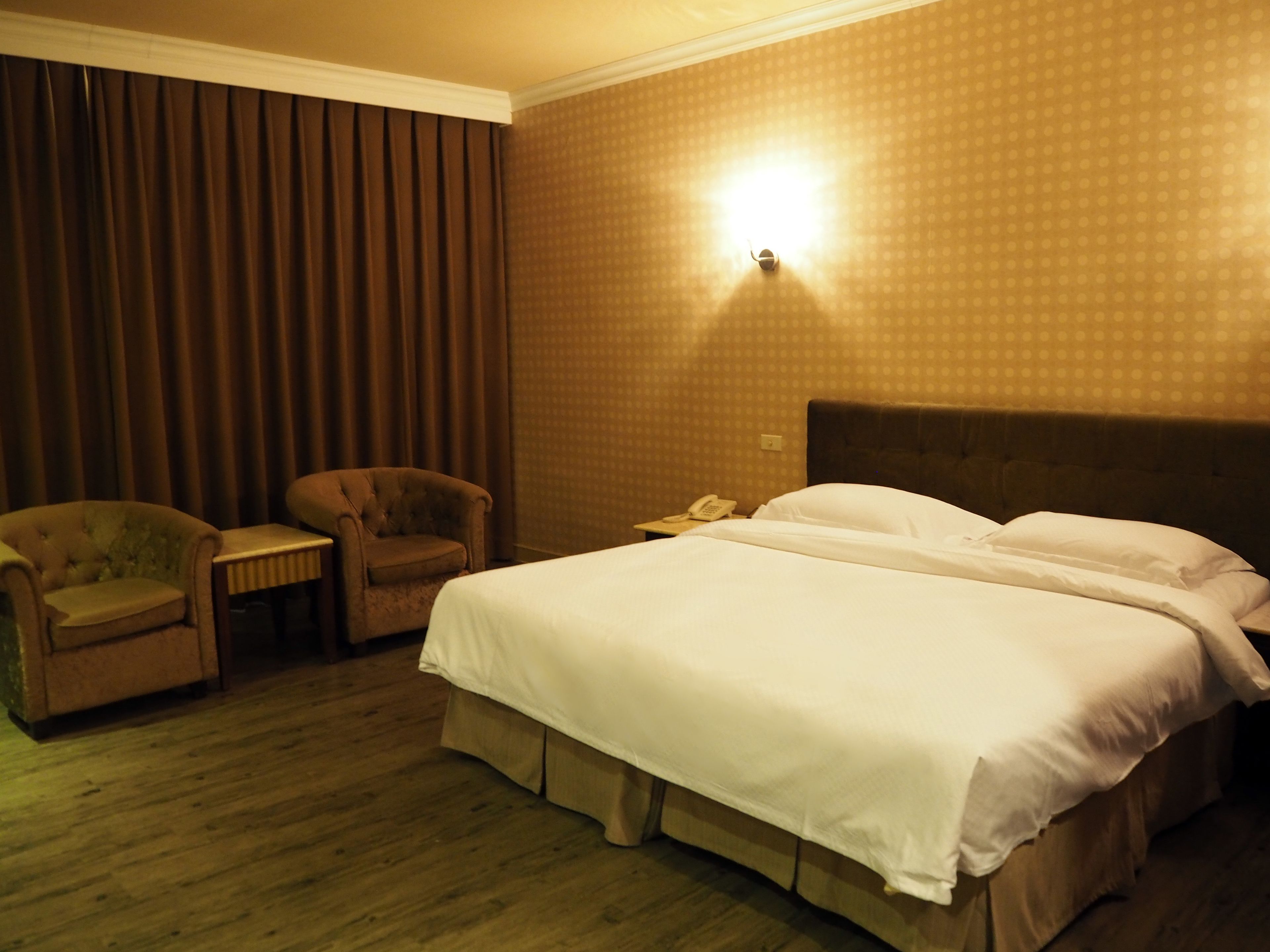 Hotellihuone, jossa on suuri sänky, kaksi nojatuolia, pieni pöytä ja yöpöytä, jossa on puhelin.