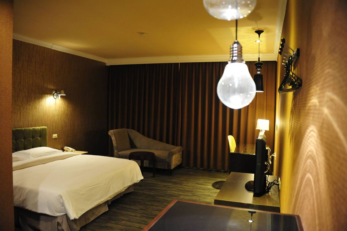 A hotel room with two beds, a desk, a chair, and a large window with curtains.