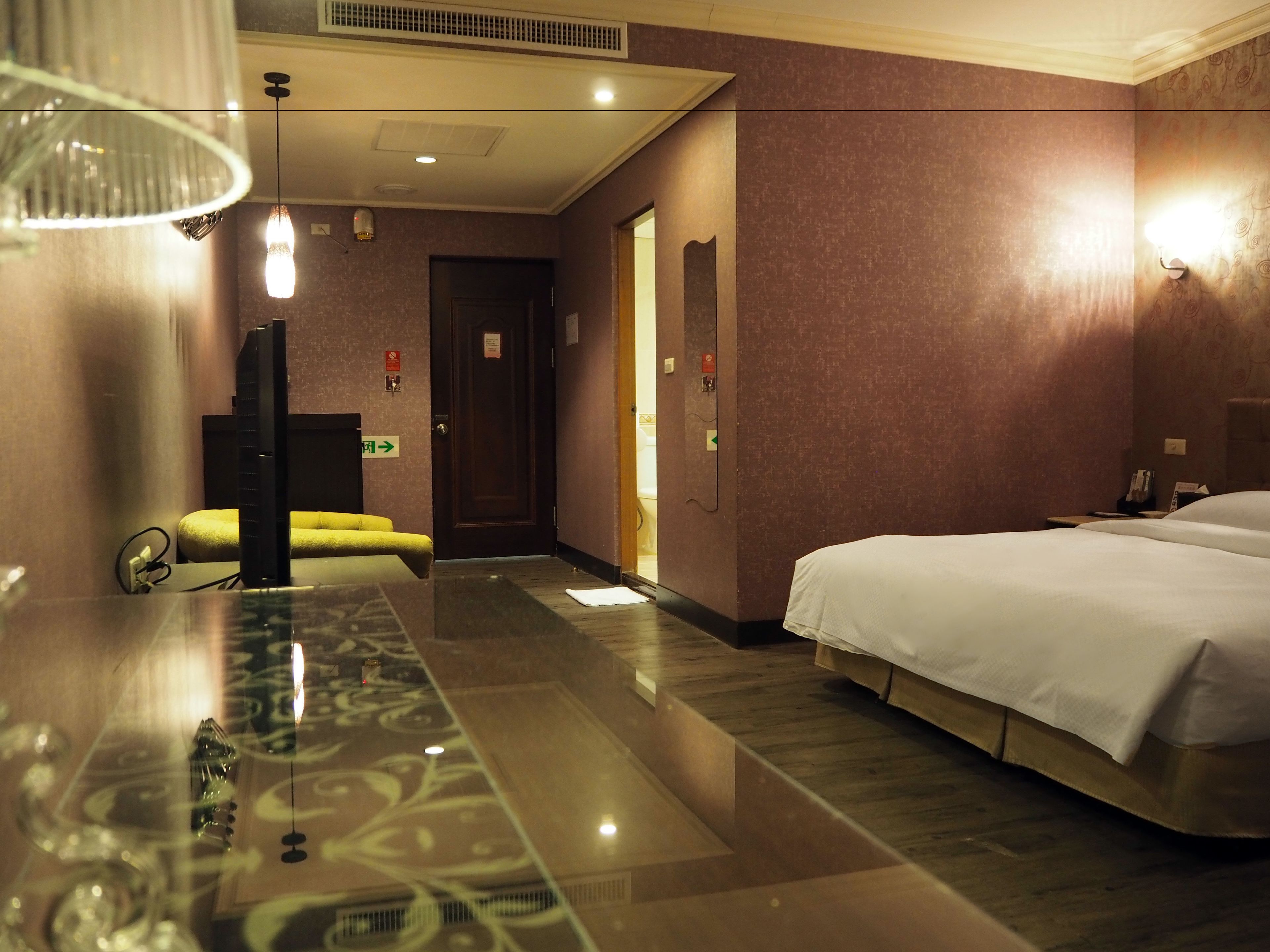 Una habitación de hotel con una cama grande, un escritorio con ordenador, una silla amarilla y un espejo.