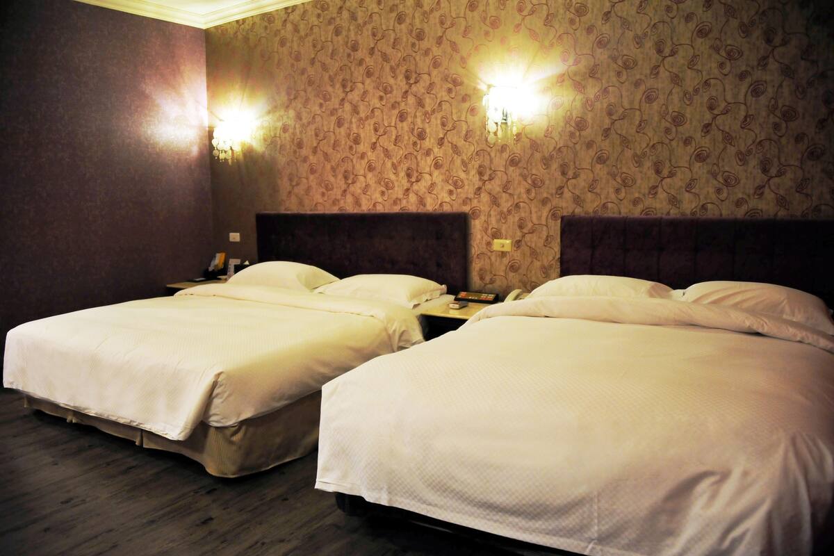A hotel room with two beds, a wooden floor, and patterned wallpaper.