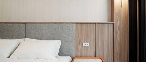 A hotel room with a bed, a nightstand with drawers, a wall-mounted light, and a power outlet.