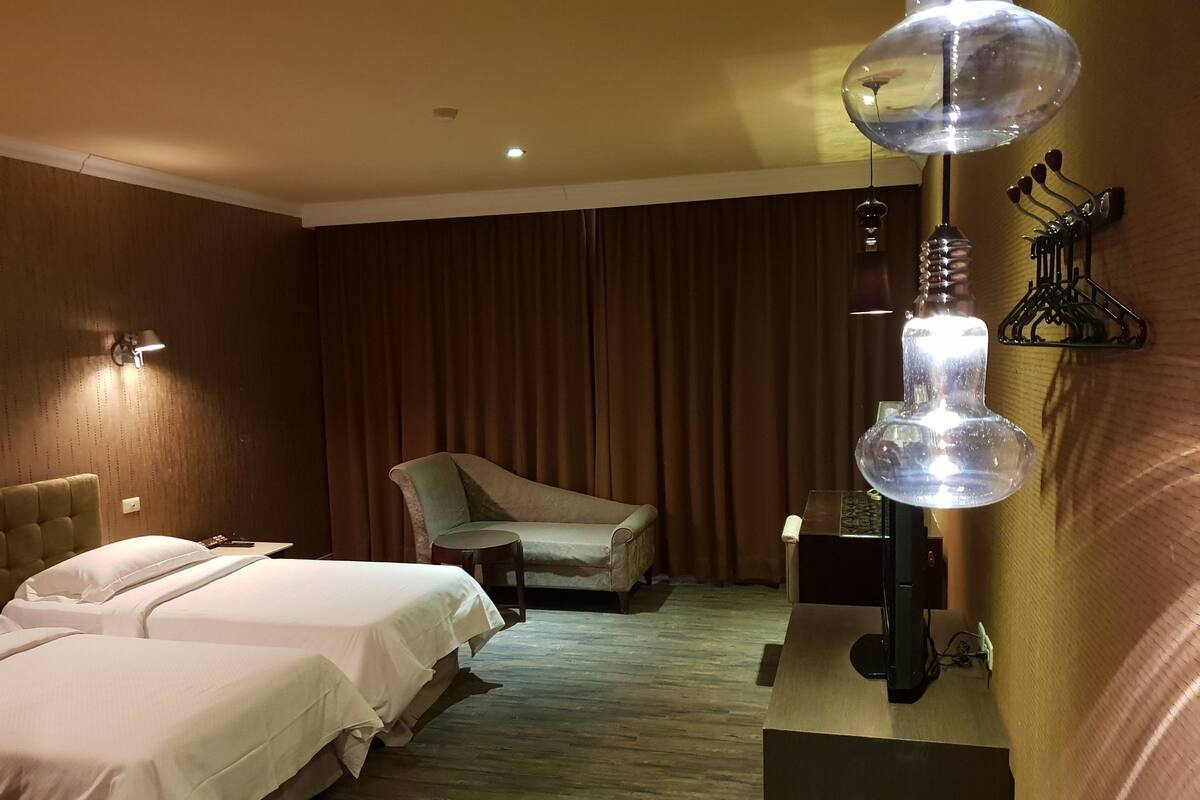 A hotel room with two beds, a chair, a desk, and a unique spherical lamp.