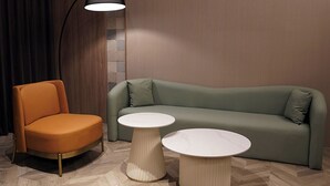 A modern living room with a green sofa, an orange armchair, and two round tables. - The Riverside Hotel & Motel (Kaohsiung)