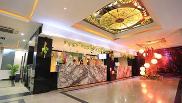 A hotel lobby with a reception desk, a large decorative ceiling, and a modern floor design.