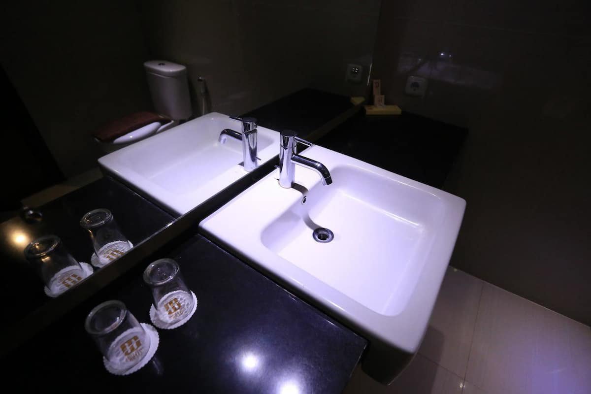 Casa de banho com duas pias, espelho e bancada preta.