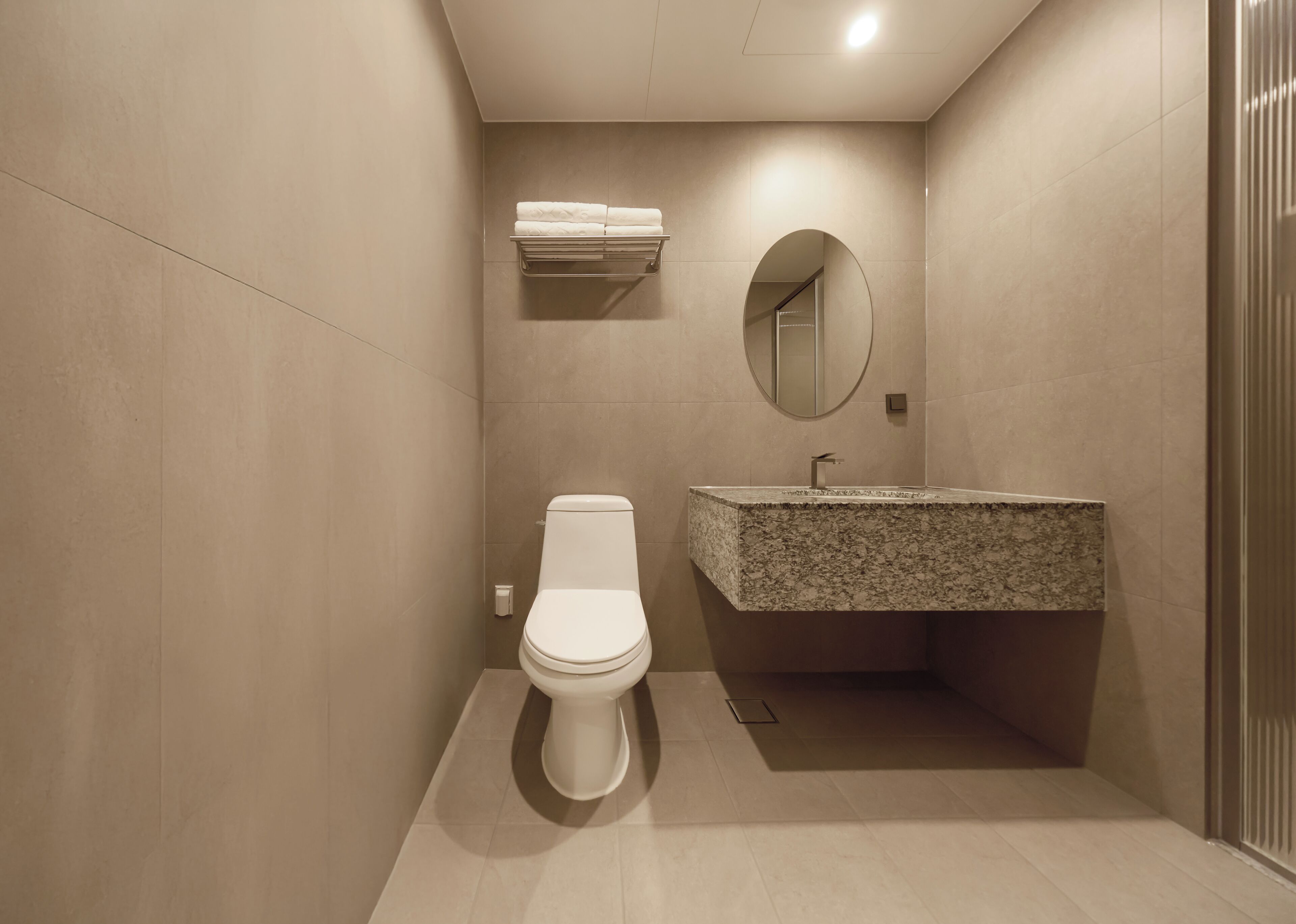 Un baño moderno con inodoro, lavamanos de encimera de granito y espejo en la pared.