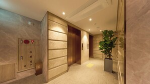 A modern elevator with a digital display and emergency button, a hallway with a marble floor, and a potted plant. - Capace Hotel (Seoul)