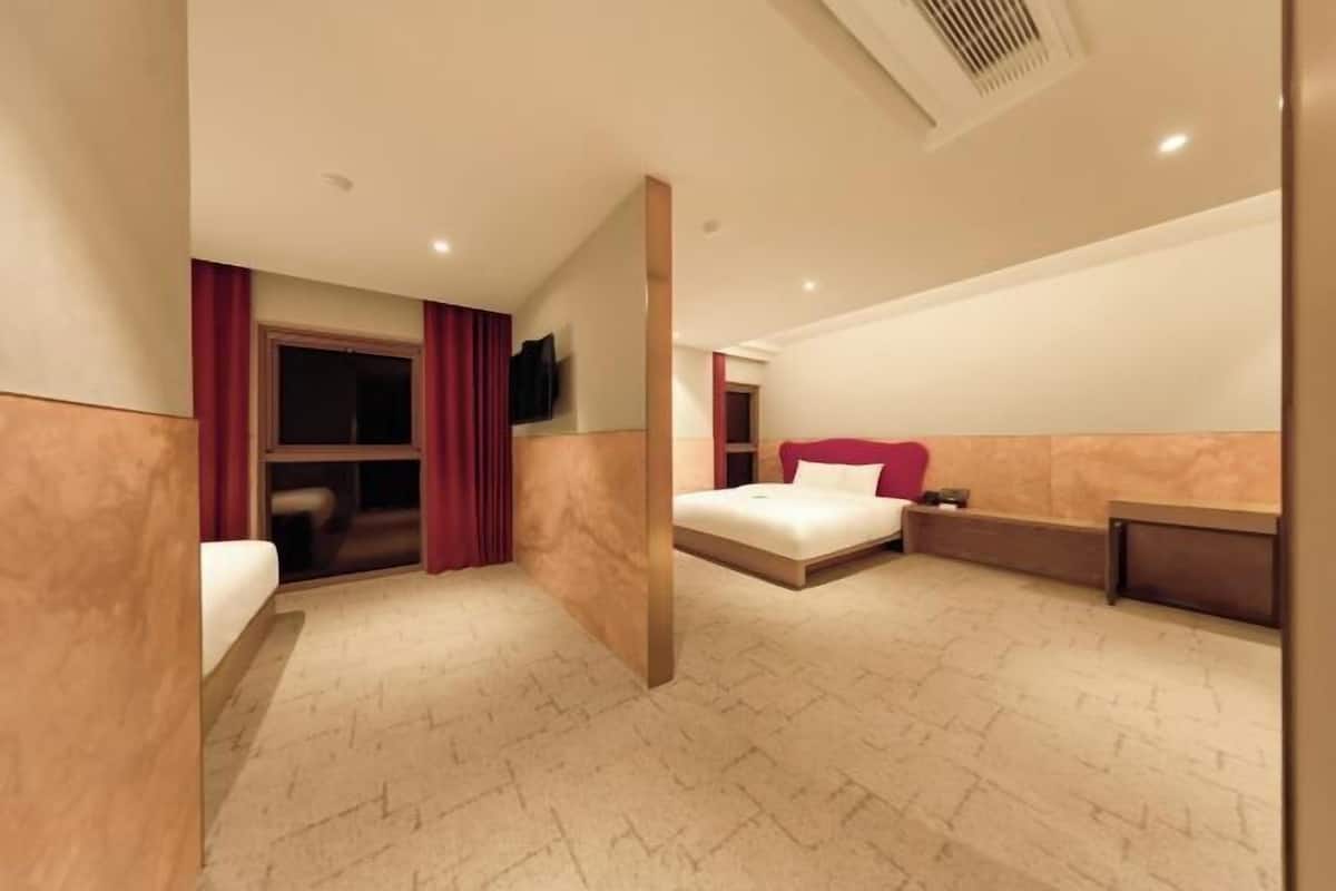 Quarto de hotel com cama, escrivaninha, televisão e janela com cortinas.