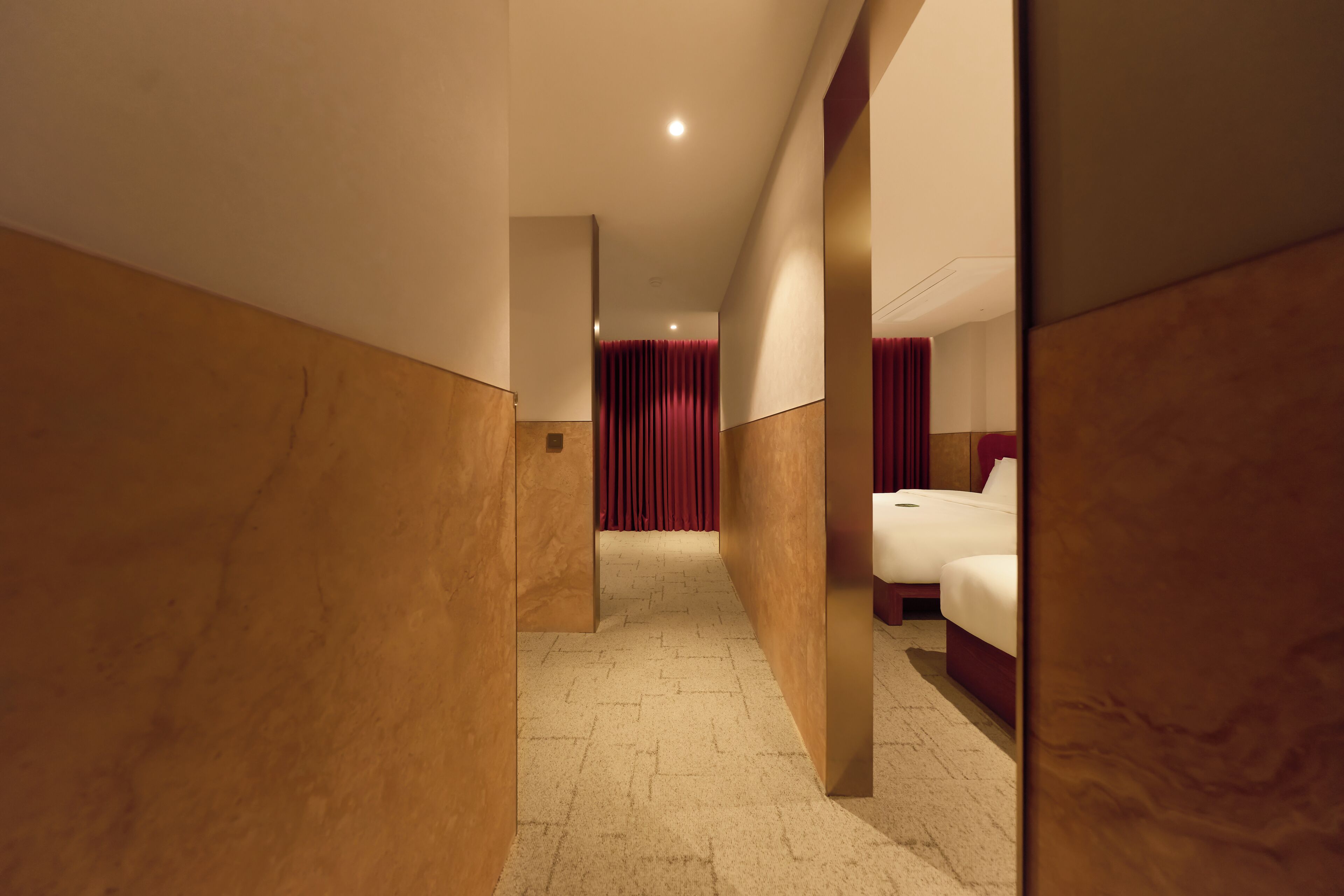 A hotel corridor with a carpeted floor, wooden walls, and a bed with white bedding.