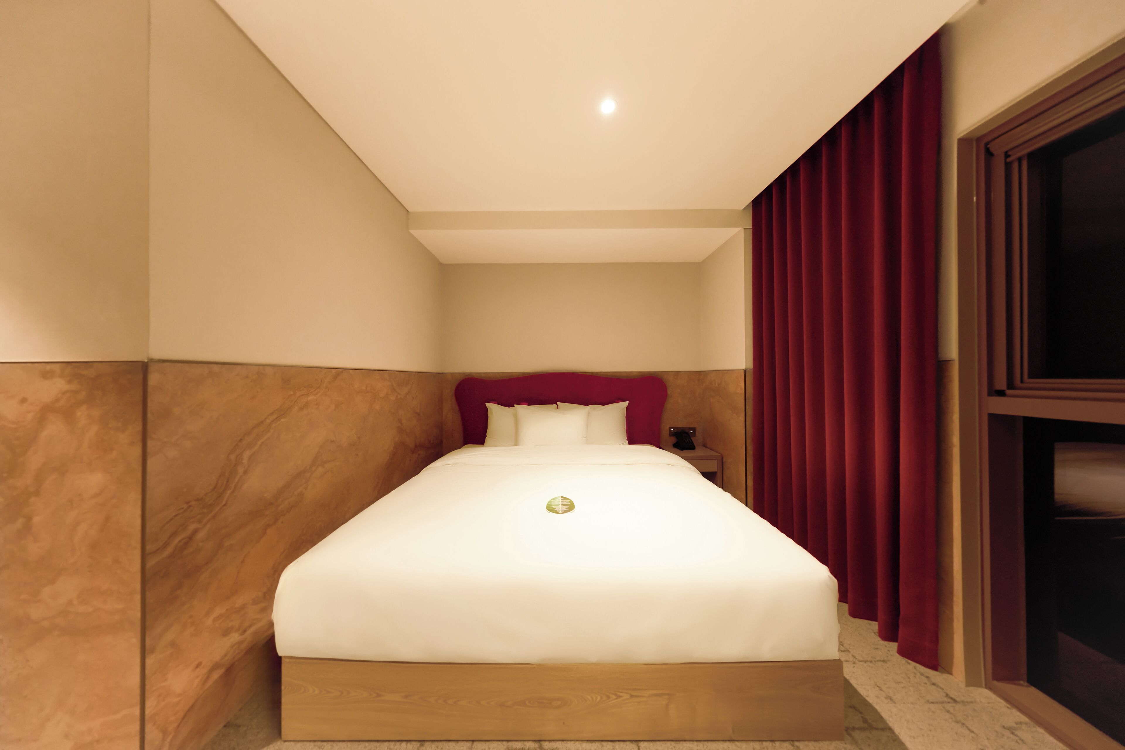 A neatly made bed with a red headboard in a room with wooden paneling and a red curtain.