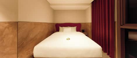 A neatly made bed with a red headboard in a room with wooden paneling and a red curtain.