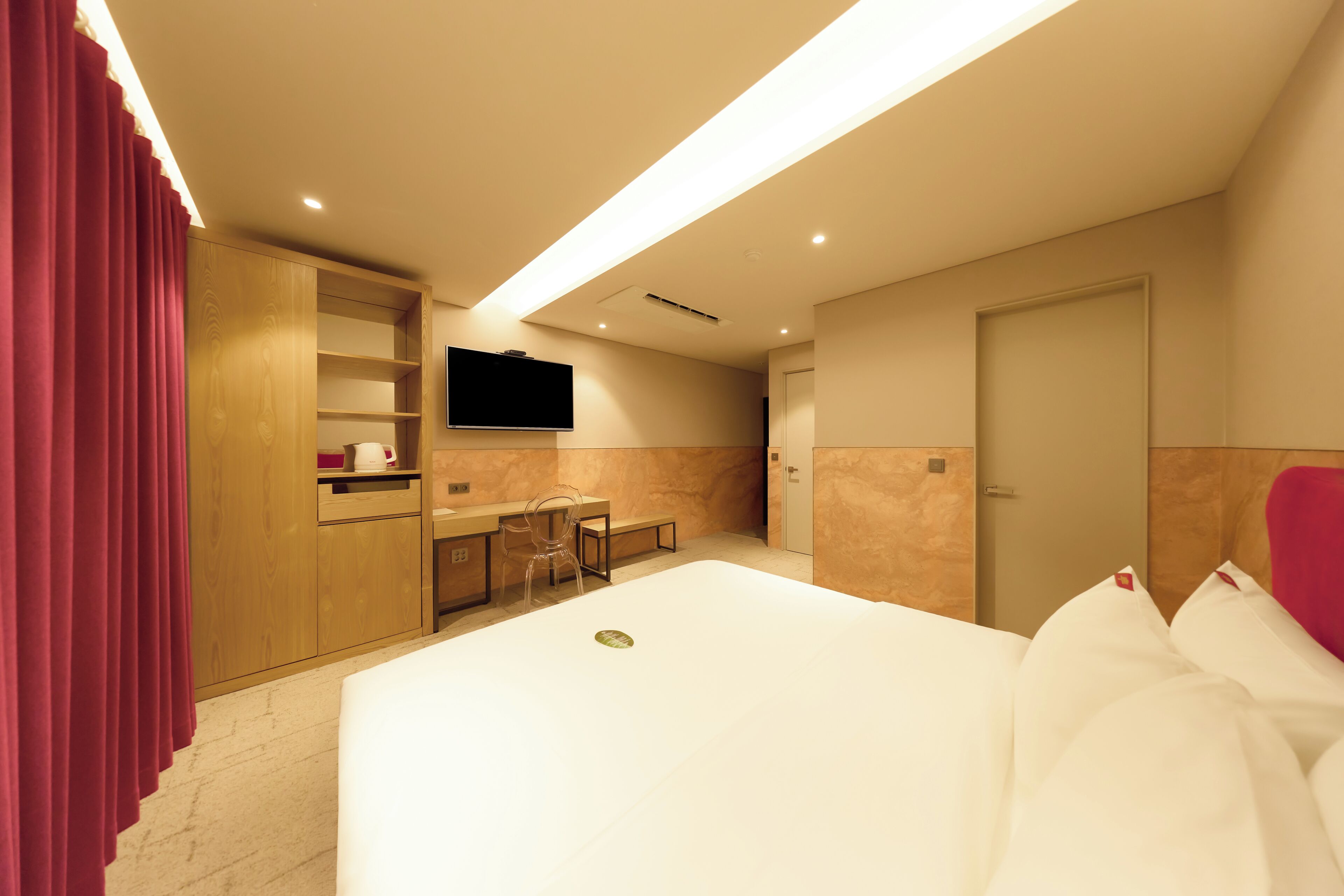 A hotel room with a large bed, a desk, a chair, a television, and a wardrobe.