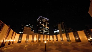 A nighttime view of a plaza with a checkered floor, illuminated by street lamps, and a tall building with lit windows in the background. - Capace Hotel (Seoul)