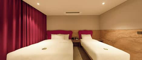 A hotel room with two beds, red curtains, beige walls, and a wooden floor.