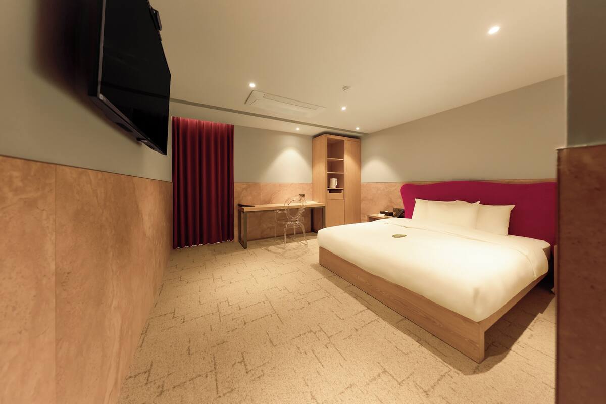A hotel room with a bed, a desk, a wardrobe, and a TV mounted on the wall.