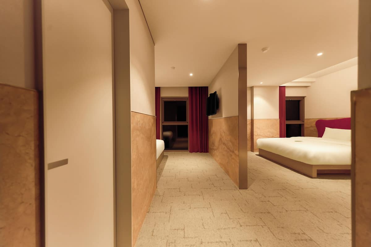 A hotel room with a bed, a TV mounted on the wall, and a door leading to another room.