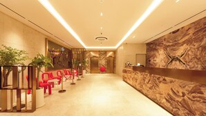 A hotel lobby with a marble reception desk, red chairs, and potted plants. - Capace Hotel (Seoul)