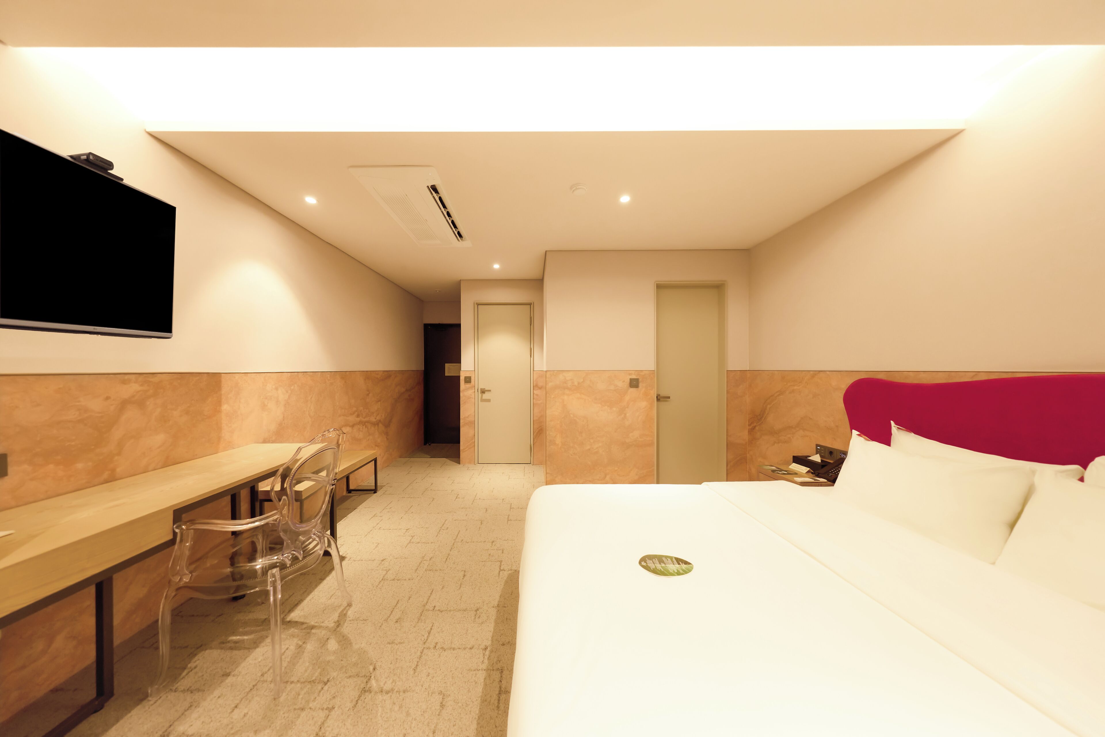 Habitación de hotel con cama, escritorio y silla. Hay un televisor montado en la pared y una puerta que da a otra habitación.