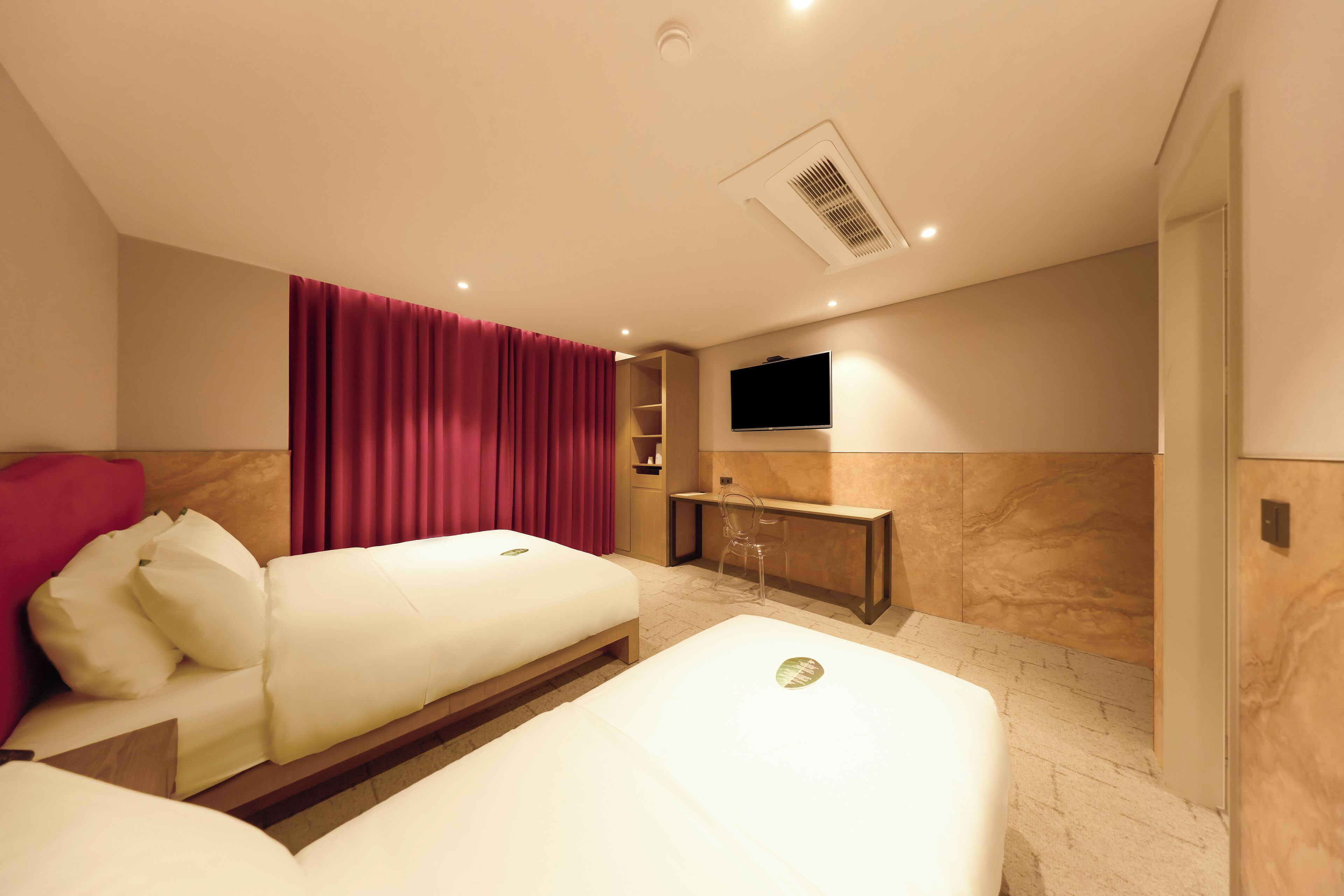 A hotel room with two beds, a TV, a desk, and a red curtain.