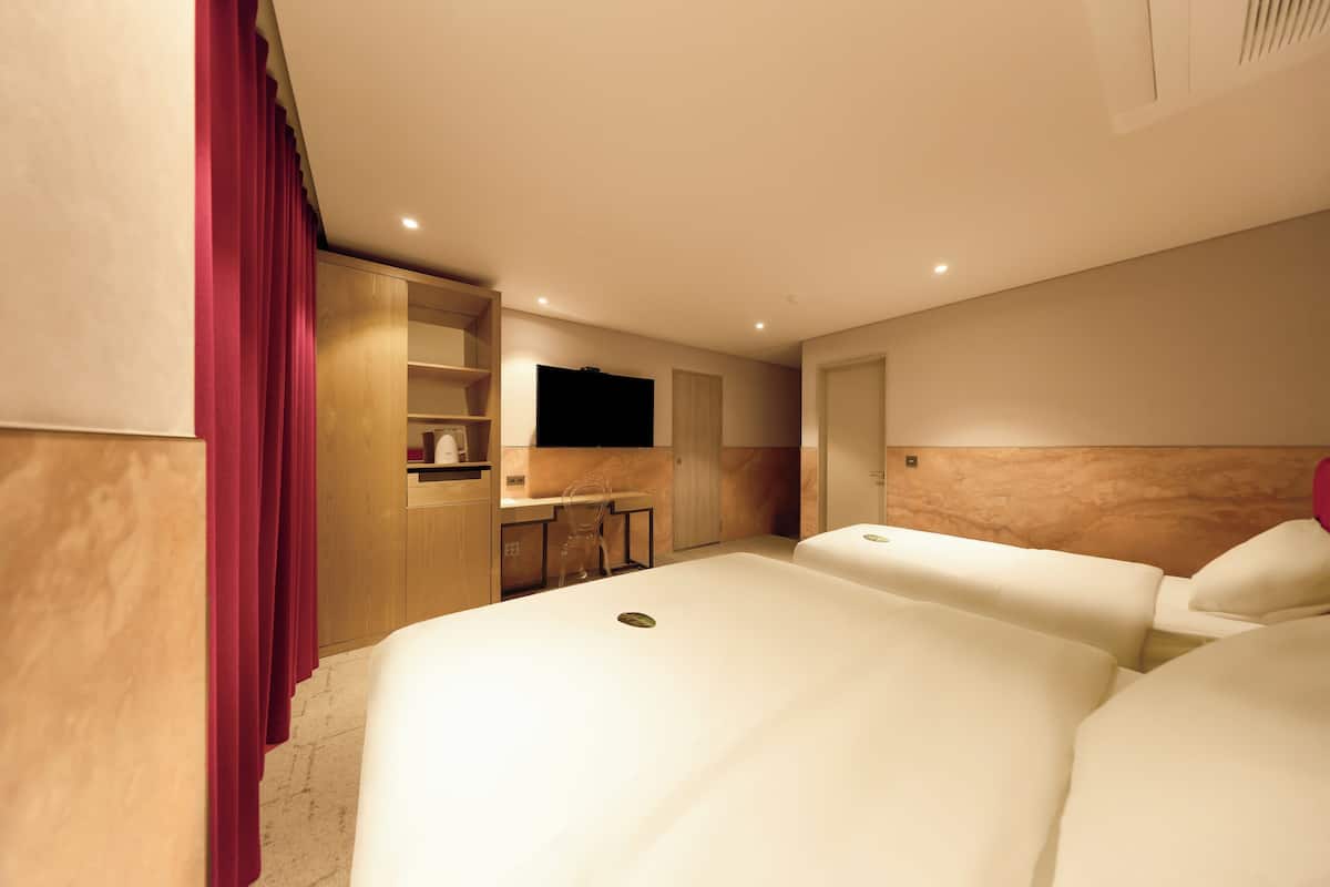 A hotel room with two beds, a desk, a mirror, and a TV.