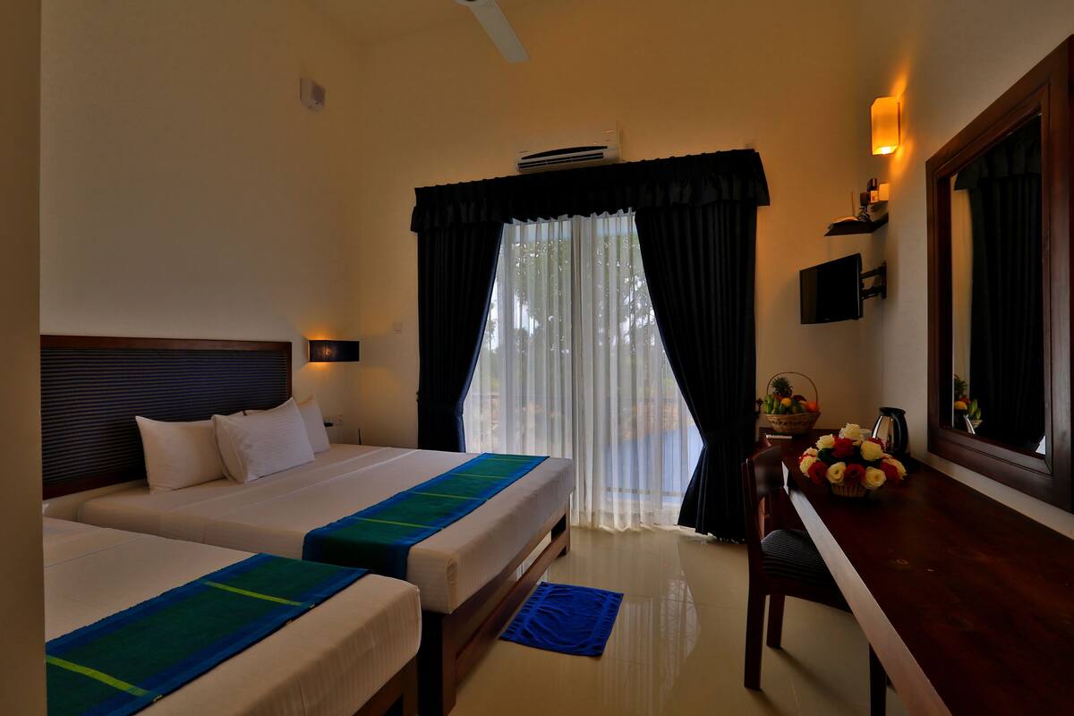 Habitación de hotel con dos camas, un escritorio, una silla, ventana con cortinas y televisor montado en la pared.