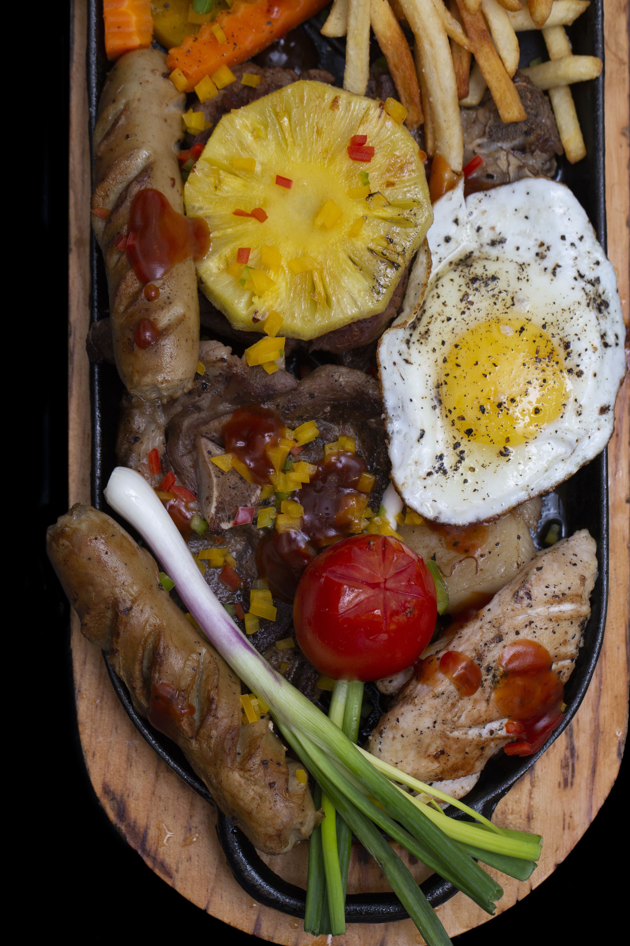 A tray of food including sausages, steak, eggs, and vegetables.