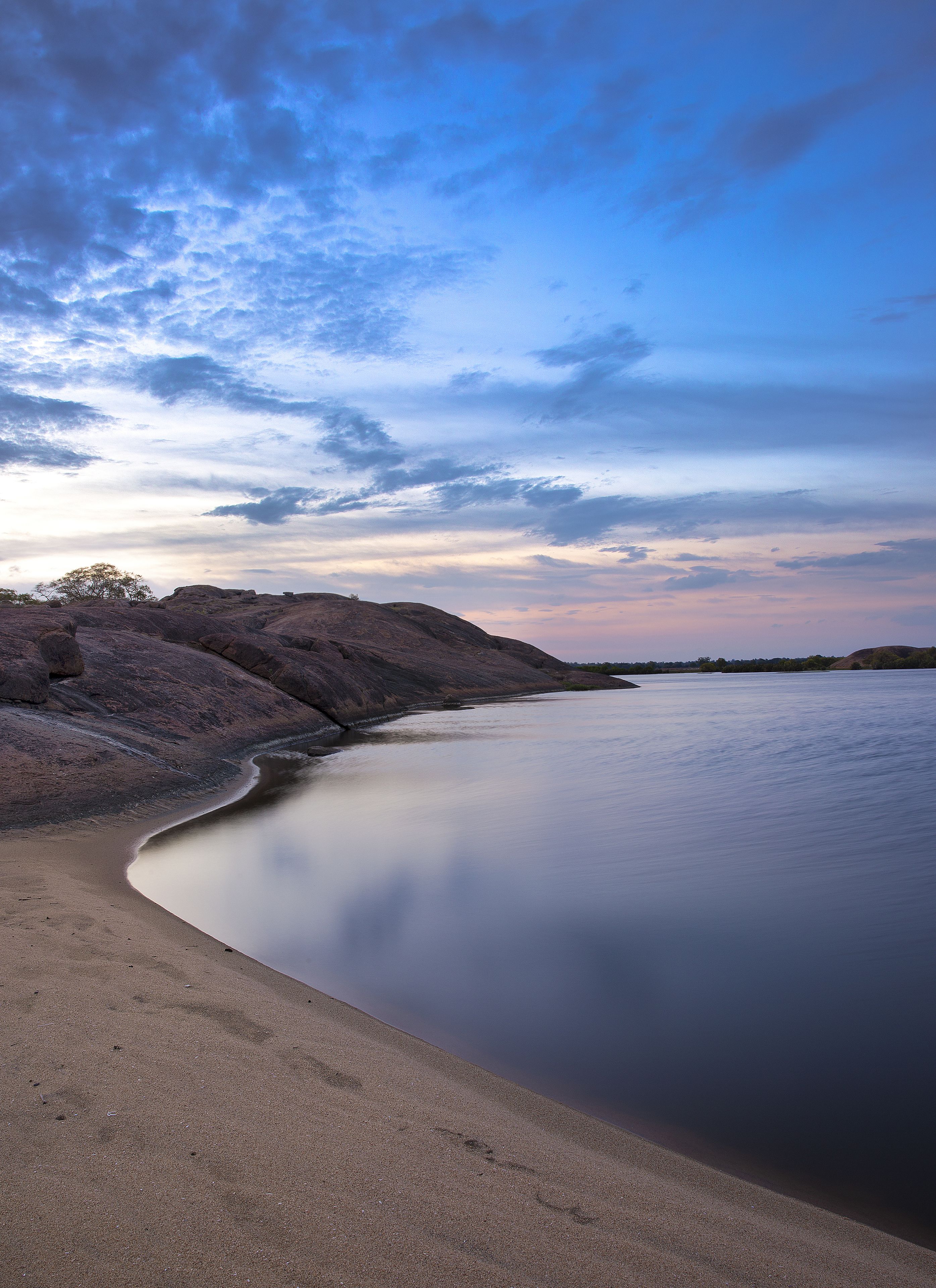 A calm beach with a clear sky and rocky terrain.