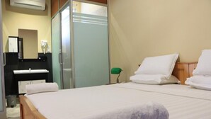 A hotel room with a bed, a bedside table, a mirror, a wardrobe, and a small green lamp.
