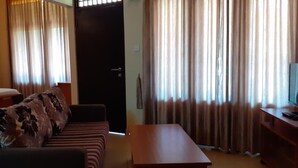 A hotel room with a bed, a sofa, a table, and curtains.