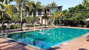 A rectangular pool with clear blue water, surrounded by palm trees and a building with balconies.