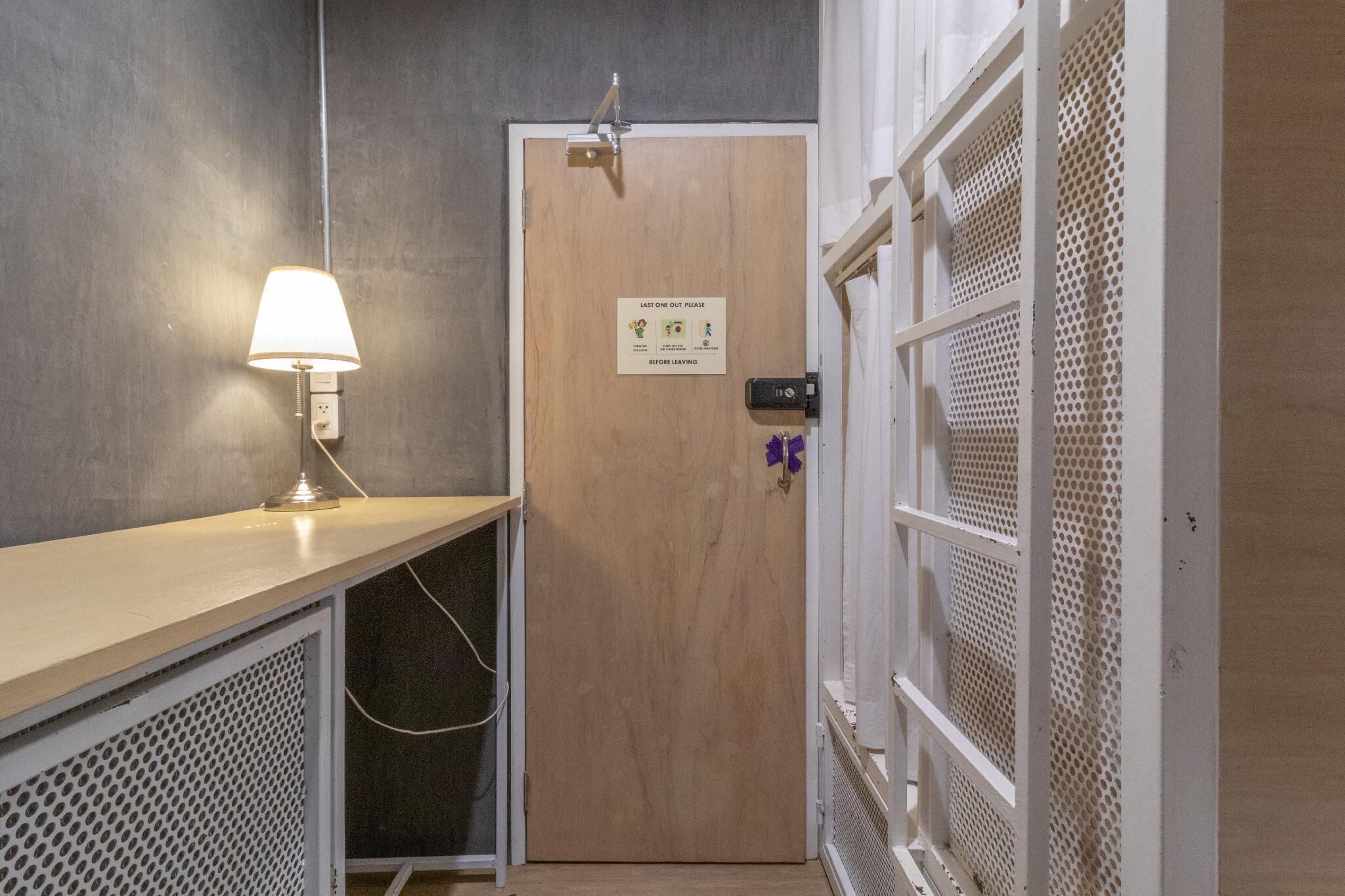 Et hotelværelse med en trædør, en vægmonteret lampe og en hvid netvæg.