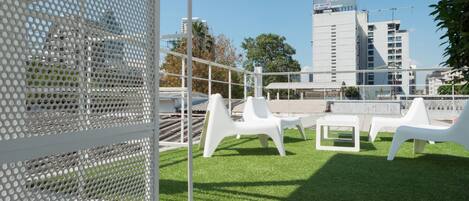 Eine Dachterrasse mit weißen Stühlen und einem weißen, gelochten Metallzaun.