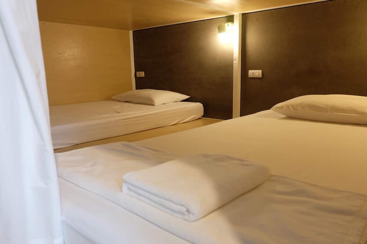 A hotel room with two single beds, each with white linens and pillows, and a large bed with white linens and a pillow.