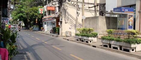 A street with a 7-Eleven store, an ATM, and a building with a concrete planter with greenery.