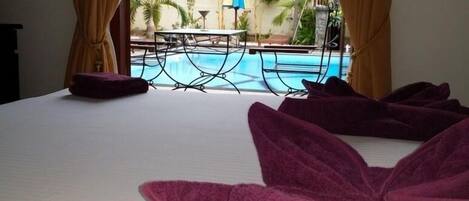 A hotel room with a bed, a view of a pool, and outdoor furniture.