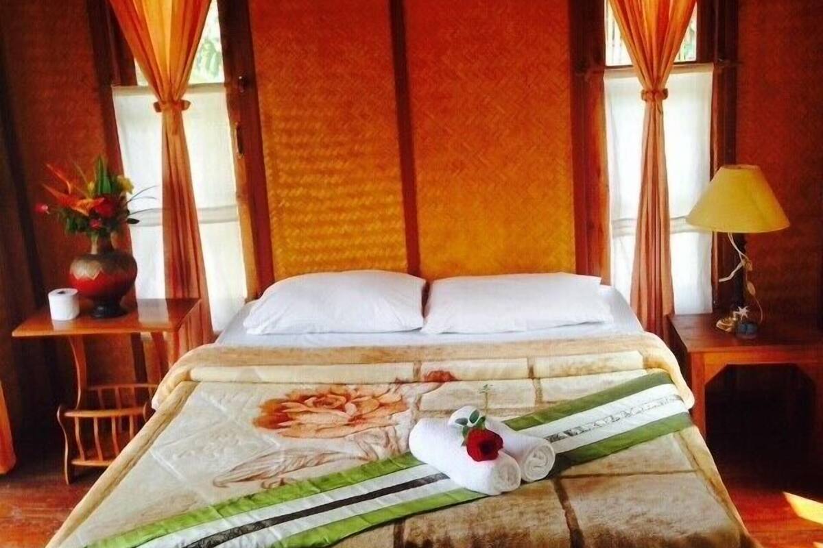 Habitación de hotel con cama, cortinas, mesita de noche con lámpara y una pequeña mesa con un florero y una planta.