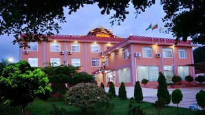 A multi-story hotel with a traditional architectural design, featuring a prominent entrance and a well-maintained garden with various shrubs and trees. - Hotel Myat Nan Taw (Loikaw)