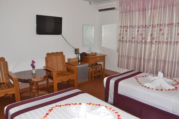 Habitación de hotel con dos camas, un escritorio, una silla, un televisor y una ventana con cortinas.