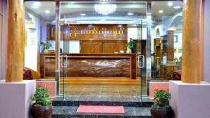 A reception area with a wooden reception desk, glass doors, and potted plants. - Hotel Myat Nan Taw (Loikaw)