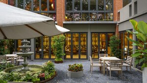 Un patio al aire libre con mesas, sillas, una fuente y plantas en macetas.