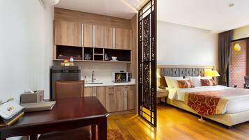 Habitación de hotel con escritorio de madera, kitchenette y cama con colcha roja y blanca.