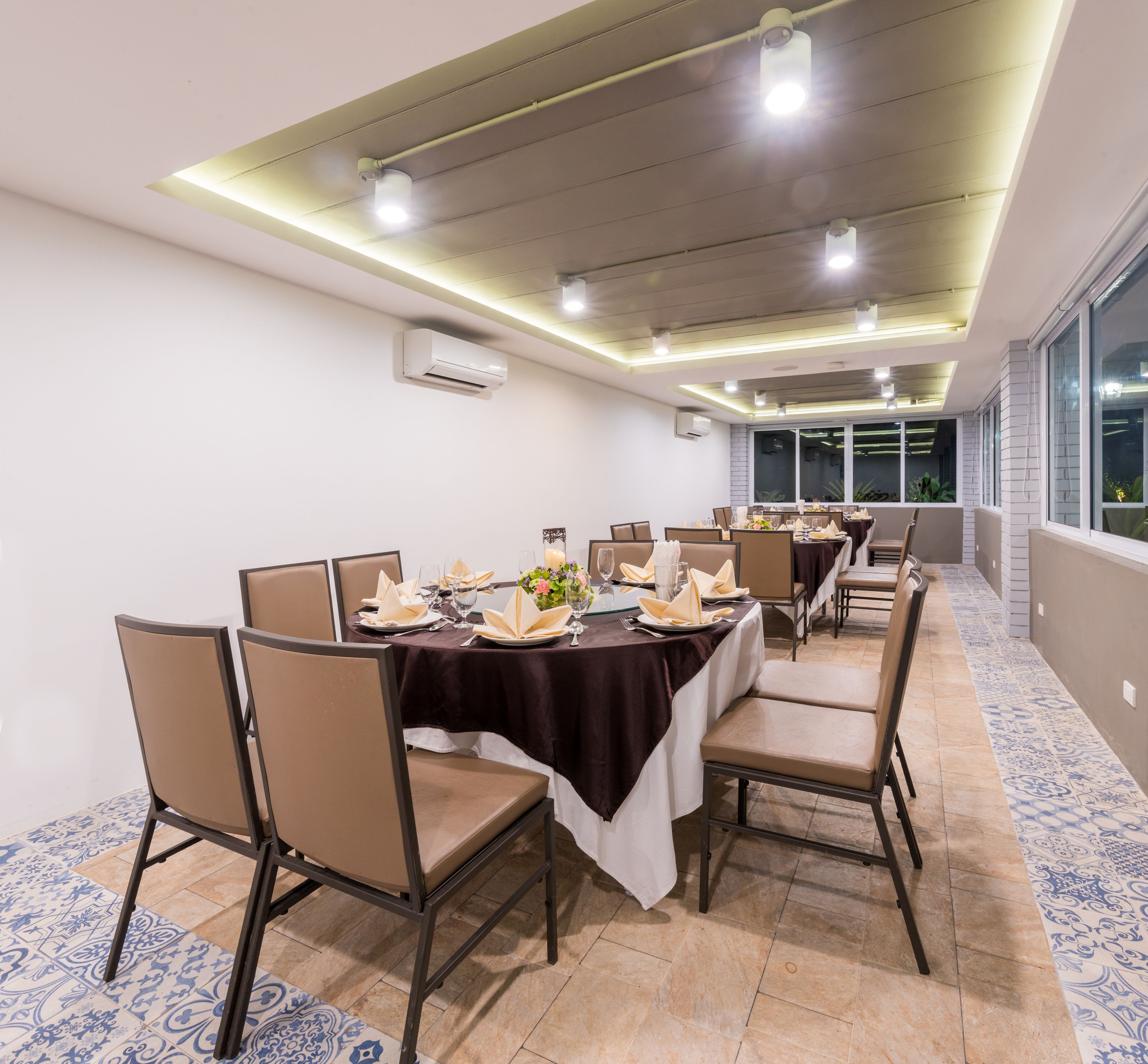 A dining area with tables set for a meal, air conditioning units on the ceiling, and large windows providing a view.