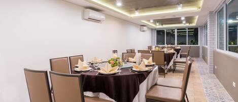 A dining area with tables set for a meal, air conditioning units on the ceiling, and large windows providing a view.