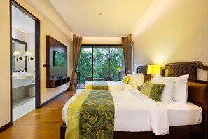 A hotel room with a large bed, a television, a balcony with a view of trees, and a bathroom with a mirror and towel rack.