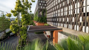Un edificio moderno con fachada ornamentada, una zona de estar al aire libre techada y abundante vegetación.