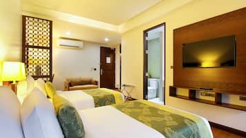 A hotel room with two beds, a TV, an air conditioning unit, and a small seating area.