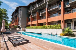 Un moderno edificio de apartamentos con piscina, sillas de descanso y fachada de ladrillo.
