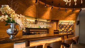 Zona de bar con techo de madera, taburetes, una estantería para vinos y un jarrón con flores.